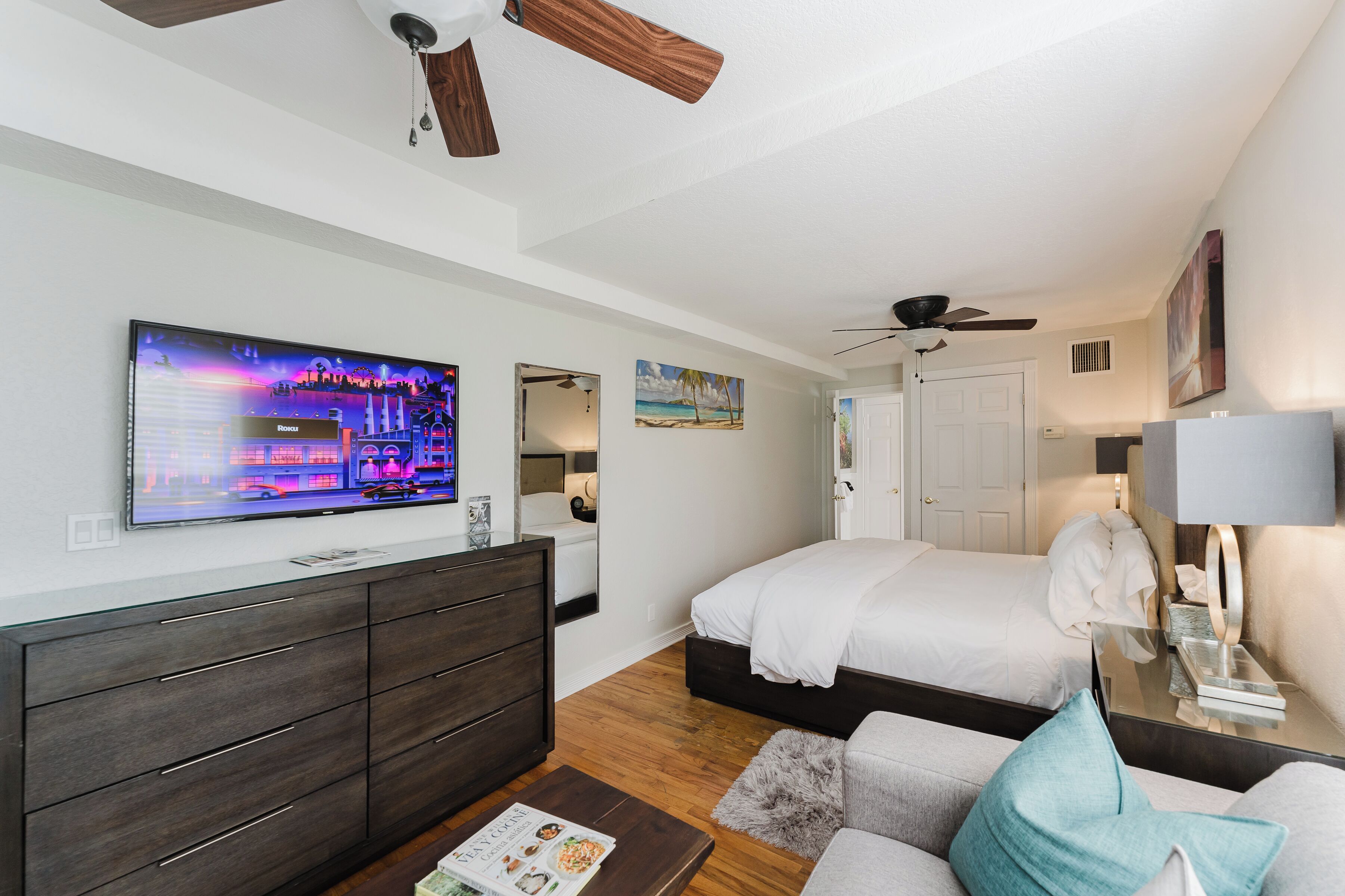 Une chambre d’hôtel moderne équipée d’un grand téléviseur à écran plat, d’un lit, d’un canapé, d’une commode et d’un ventilateur de plafond.