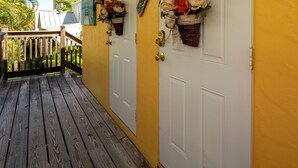 Een houten veranda met een gele muur en witte deuren, elk versierd met een bloemstuk.