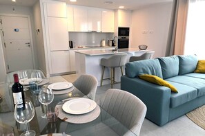 A modern kitchen with white cabinets, a central island, and a dining area with a glass table set for two.