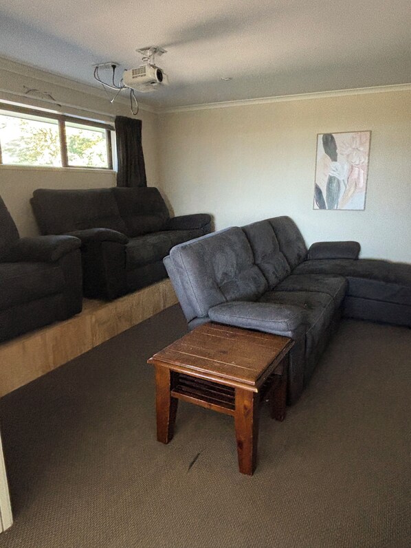 Ein Wohnzimmer mit einem Ecksofa, einem Holztisch und einem Deckenprojektor.
