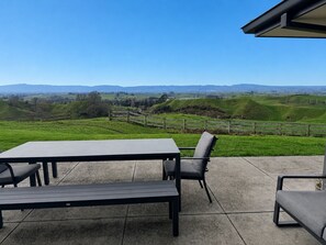 A patio with a table and chairs, a view of rolling hills, and a wooden fence.