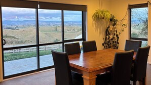 Zona pranzo con un tavolo grande e sedie, ampie finestre con vista sul paesaggio e una pianta pensile.