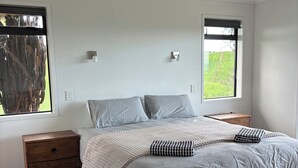 Una camera da letto con un letto, due comodini, una lampada da comodino, una finestra e vista su del verde all'esterno.
