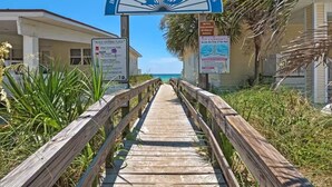 A wooden boardwalk leading to a beach entrance with a sign reading "Bay County Public Beach Access".