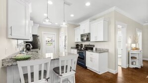 A kitchen with white cabinets, granite countertops, a dining area with white chairs, and a microwave.