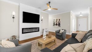 A modern living room with a flat-screen TV, fireplace, ceiling fan, and a cozy seating area with sofas and a coffee table.