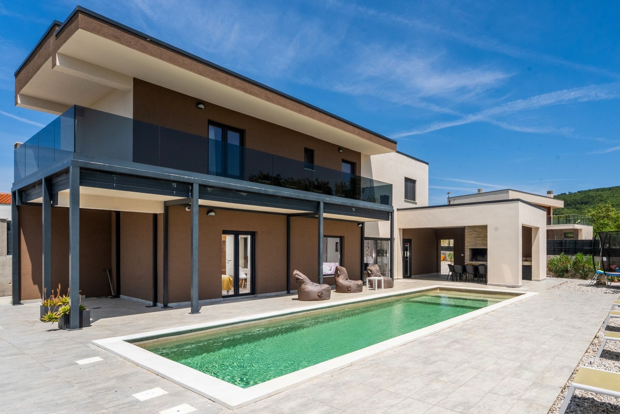 A modern two-story house with a swimming pool, outdoor seating, and a covered patio area.