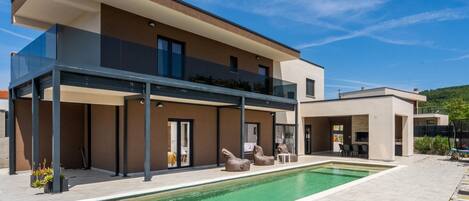 A modern two-story house with a swimming pool, outdoor seating, and a covered patio area.