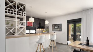 Una cocina moderna con una isla central, taburetes blancos y luminarias colgantes.