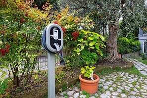 An electric vehicle charging station in a garden with a potted plant nearby.