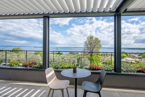 A balcony with a view of a lake, two chairs, and a small table with a plant.