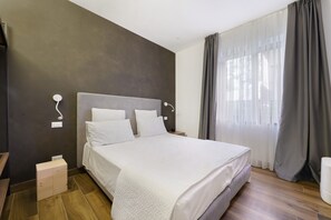 A modern bedroom with a large bed, a bedside table, a nightstand, and a window with curtains.