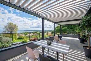 Un espacio al aire libre cubierto con una mesa, sillas, una planta en maceta y vistas al mar y al verdor.