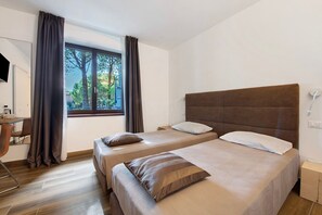 Habitación de hotel con dos camas, un escritorio y una ventana con cortinas.