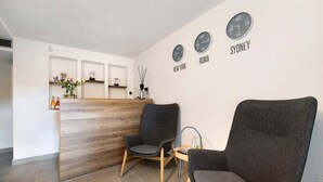 A reception area with a wooden reception desk, two grey armchairs, and wall clocks labeled with city names. - Room 'Insula Felix Matr Lake View' with Shared Terrace, Wi-Fi and Air Conditioning (Moniga del Garda)