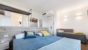 A modern hotel room with a large bed, a smaller bed, a wooden headboard, a bedside table, a mirror, and a wall-mounted light fixture.