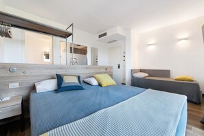 A modern hotel room with a large bed, a smaller bed, a wooden headboard, a bedside table, a mirror, and a wall-mounted light fixture. - Room 'Insula Felix Tripla Vista Lago' with Shared Terrace, Wi-Fi and Air Conditioning (Moniga del Garda)