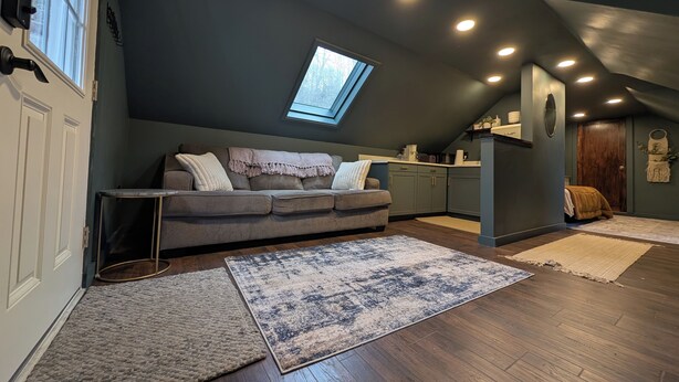 Un dormitorio tipo loft acogedor con techo inclinado, tragaluz, sofá gris y suelo de madera.
