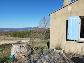 A rustic stone building with a blue shutter, a stone well, and a stone wall.