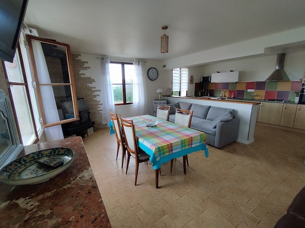 A dining area with a table and chairs, a kitchen with colorful tiles, a sofa, and a clock on the wall.