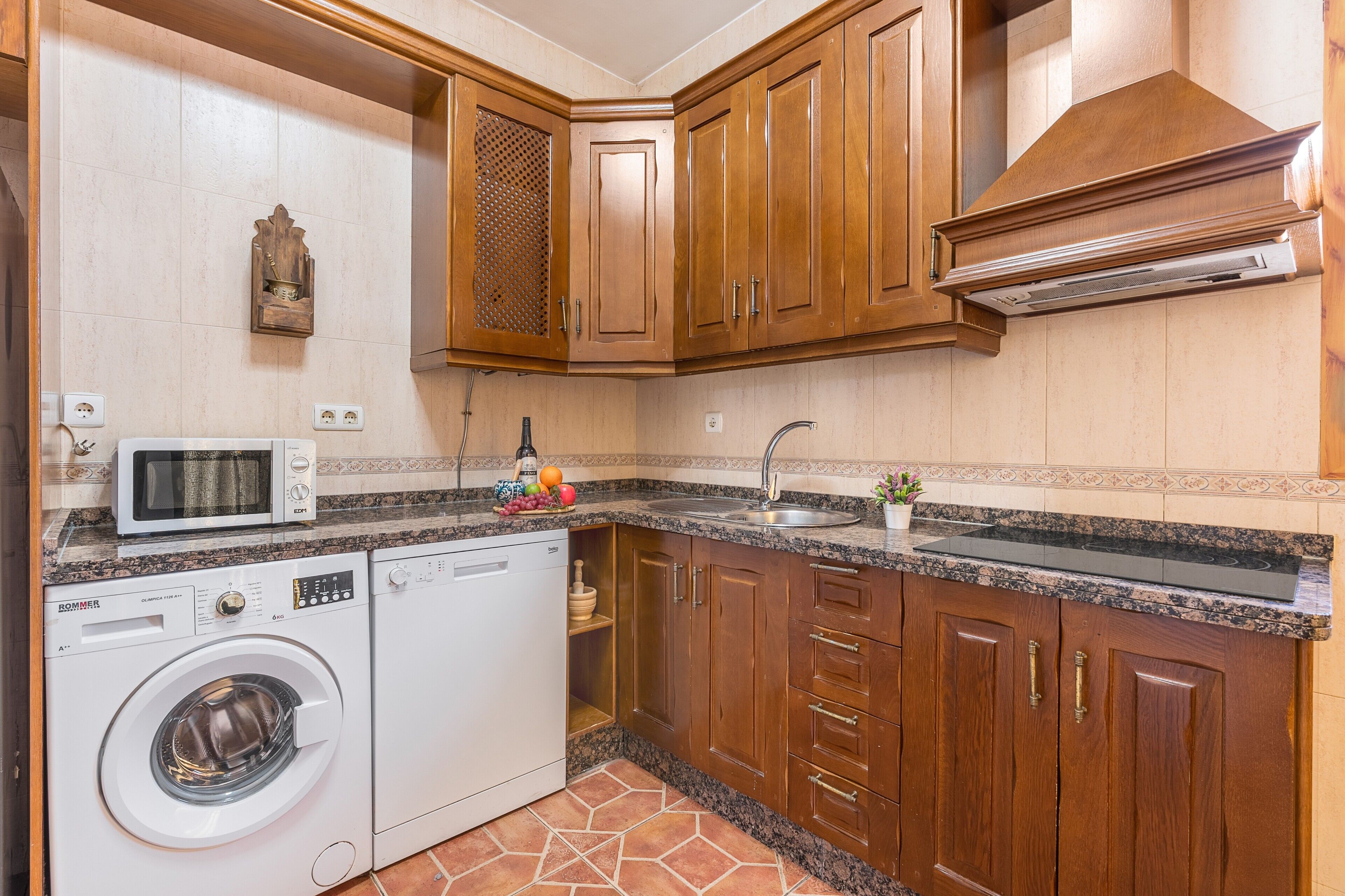 Una cocina con armarios de madera, un microondas, una lavadora y un lavaplatos.