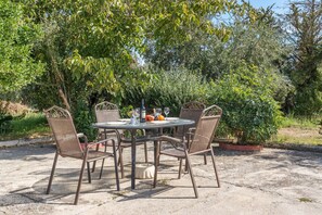 Une terrasse extérieure avec une table ronde et quatre chaises, entourée de verdure.