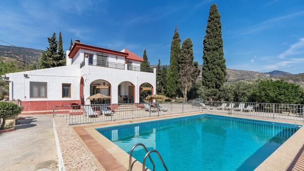 A poolside view of a two-story building with a red roof and white walls, surrounded by trees and a mountainous backdrop. - Country House 'Ana - Cortijo Puerta' with Private Pool, Wi-Fi and Air Conditioning (Órgiva)