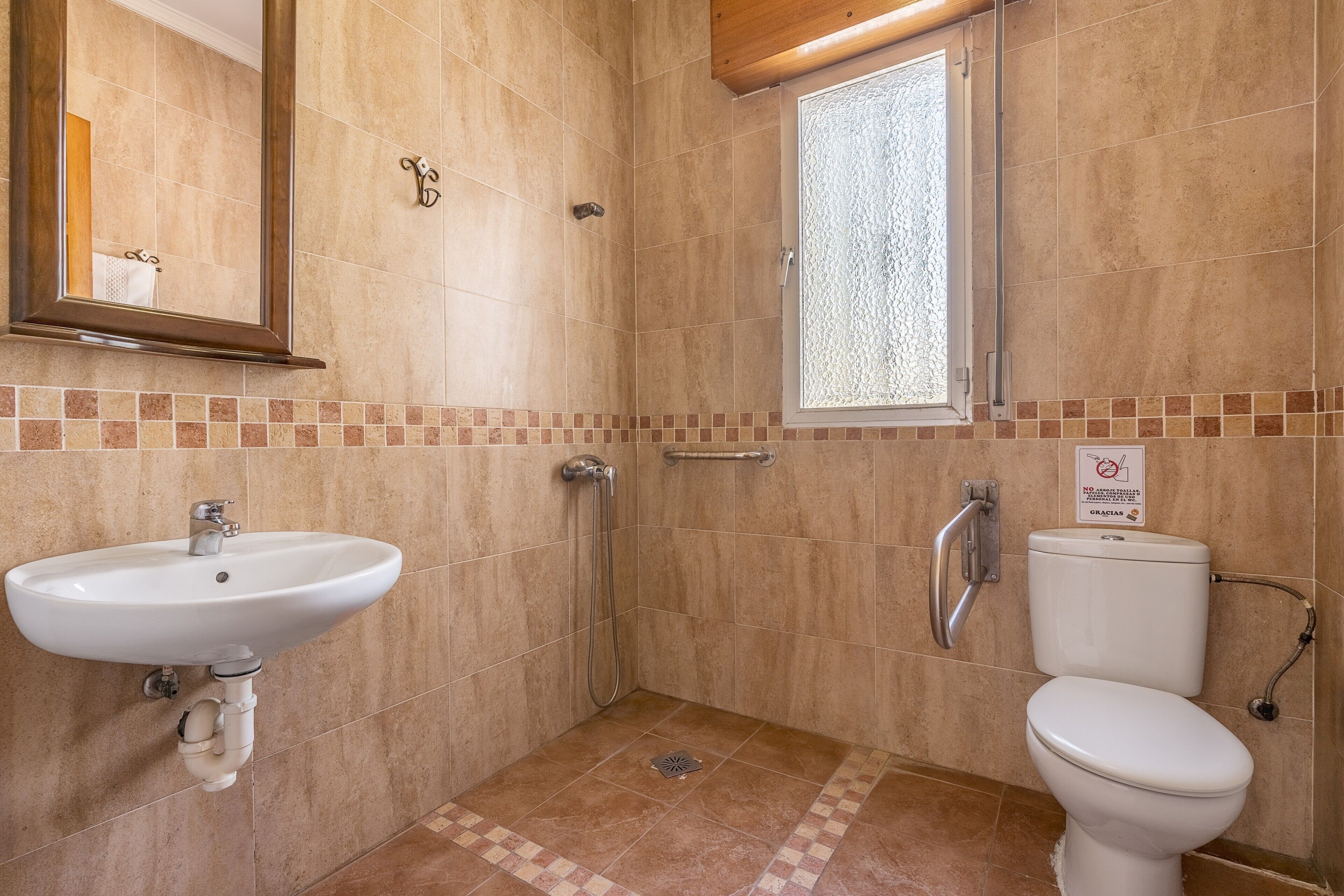 Een badkamer met wastafel, toilet, douche en een raam.