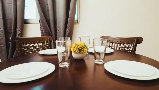 A dining table set for four with white plates, clear glasses, and a small vase with yellow flowers. - Apartments cabos 1 (San José del Cabo)