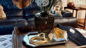 Ein Wohnzimmer mit einer dunkelbraunen Vase, die eine Pflanze und Dekoelemente enthält, einer Tablett mit Snacks und einem gemusterten Teppich.