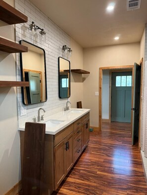 A bathroom with a double vanity, a large mirror, and a wooden floor. - Comanche Ridge Getaway Cabin: Located at the Six Star Ranch! (Llano)