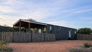Ein modernes, eingeschossiges Gebäude mit überdachter Terrasse, Holzzaun und Kiesgrundstück.