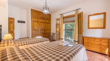 A hotel room with two beds, a wooden wardrobe, a dresser, a lamp, and a view of palm trees.