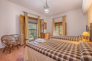Una stanza con due letti, una sedia, un comò e un balcone con tende.
