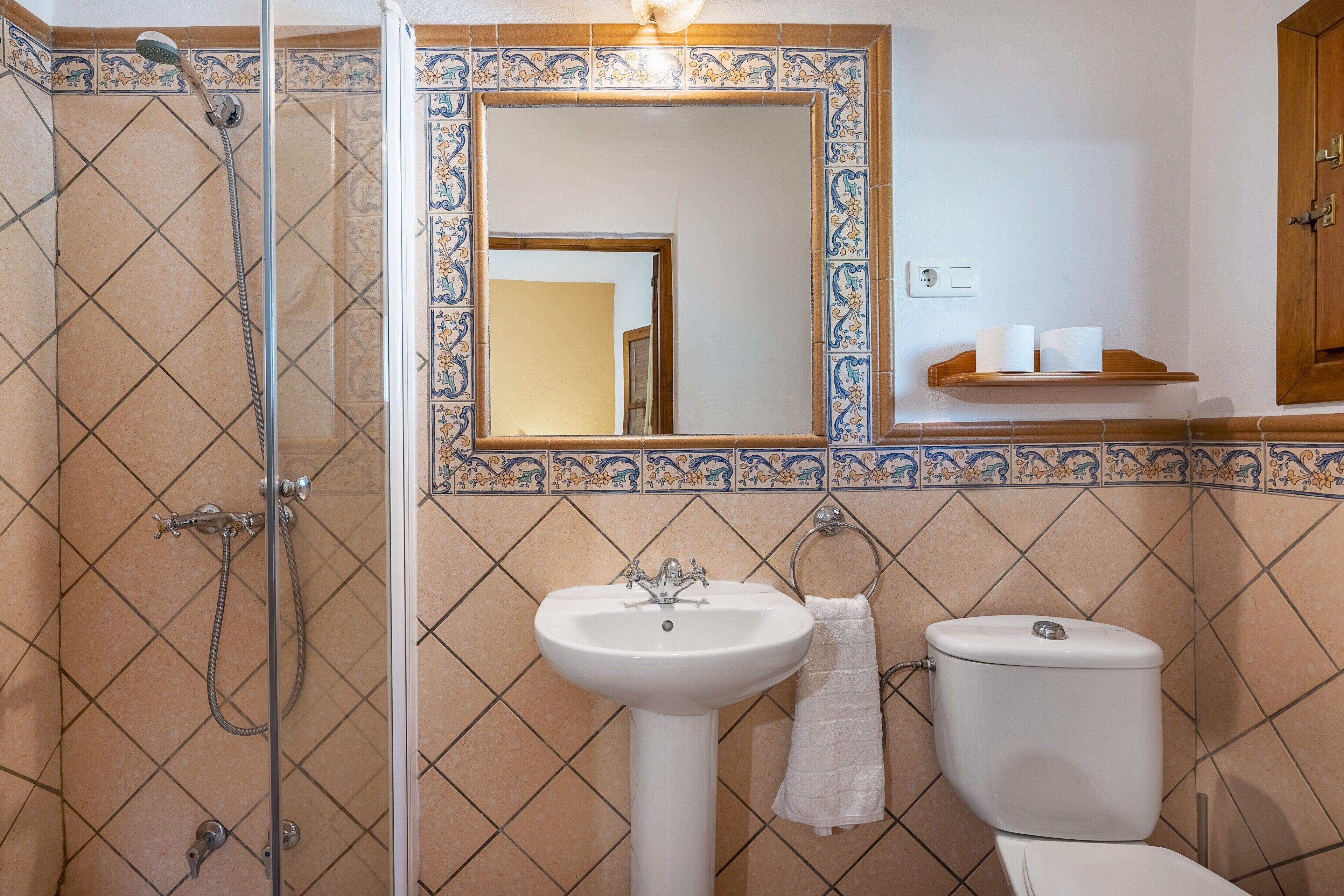 Ein Badezimmer mit Dusche, Waschbecken, Toilette und einem Spiegel mit dekorativer Fliesenleiste.