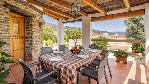 A covered patio with a checkered tablecloth, stone walls, and a wooden ceiling.