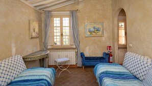 A room with two beds, a small table, a window with curtains, a radiator, and a fire extinguisher. - San Giovanni R. Apartment 1 Dantea with Private Garden, Wi-Fi, and Air Conditioning (Peccioli)