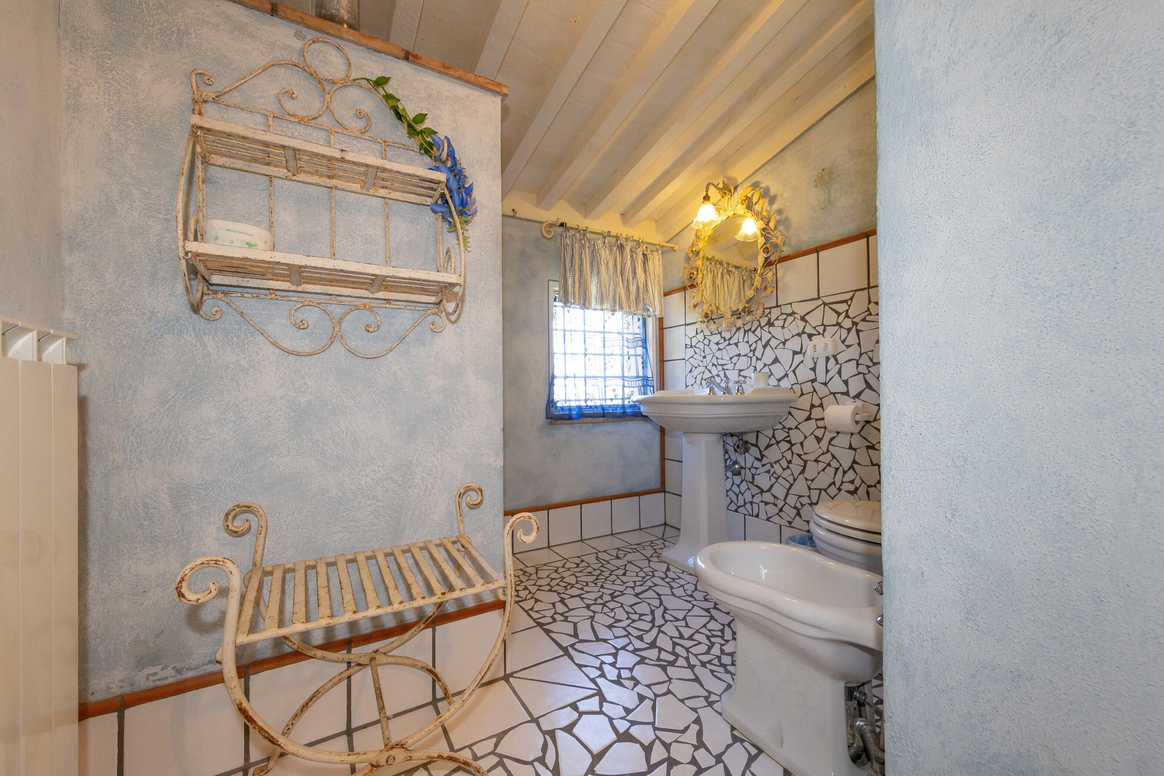 A bathroom with a tiled floor, a sink, a mirror, and a shelf with decorative items.