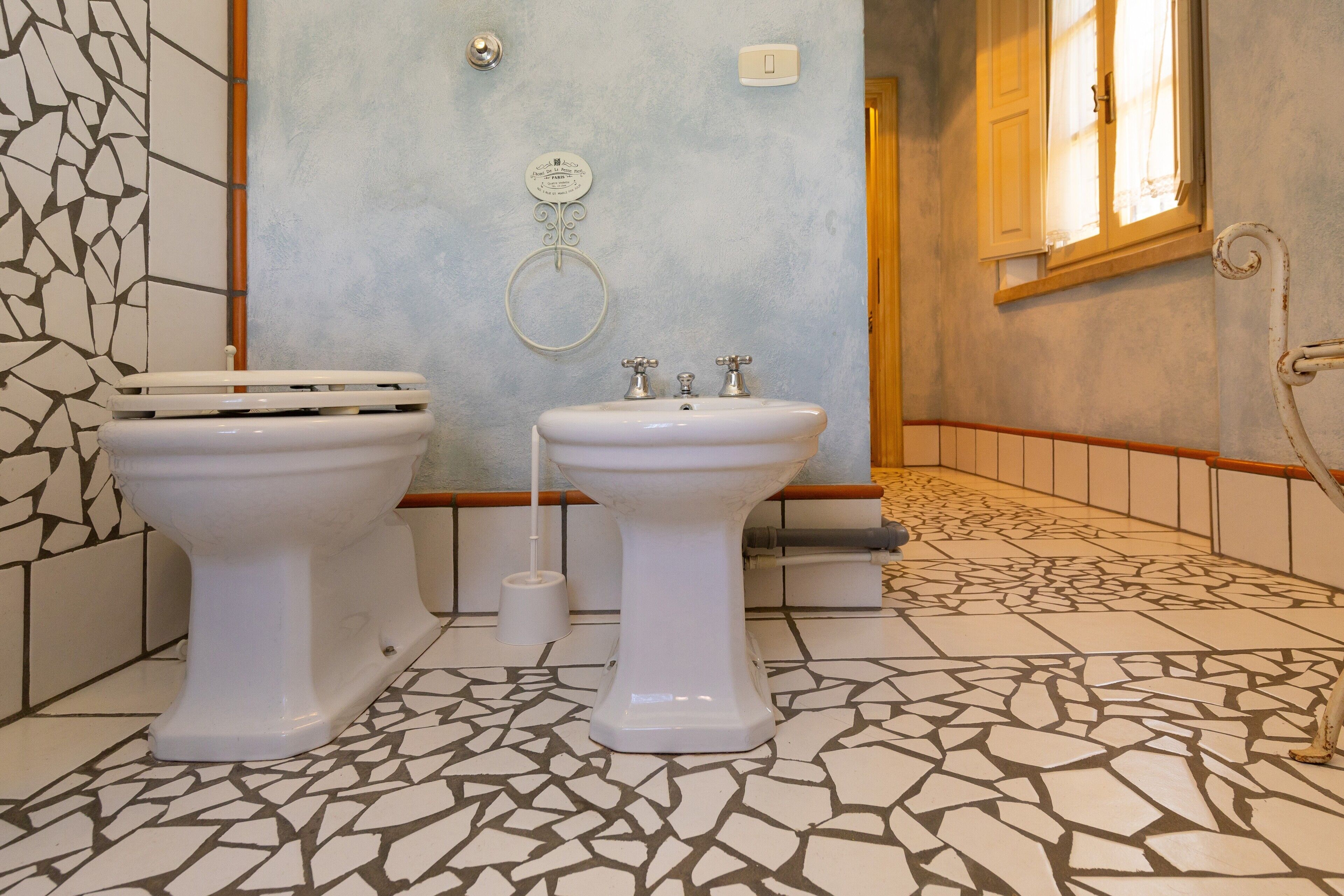 A bathroom with two toilets, a sink, a towel ring, and a patterned floor.