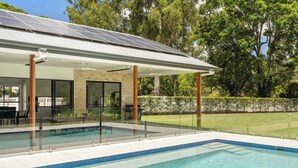 A modern outdoor pool area with a covered patio, solar panels, and a well-maintained lawn.
