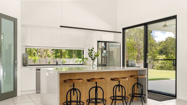A modern kitchen with a central island, bar stools, and a large window offering a view of the outdoors.