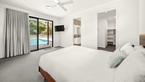 A modern hotel room with a large bed, a ceiling fan, a TV, and a view of a swimming pool.