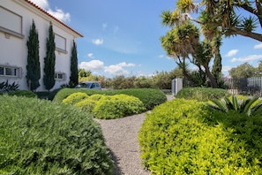 Un jardin bien entretenu, avec des haies taillées, un chemin de gravier et un bâtiment blanc surmonté d’un toit rouge.