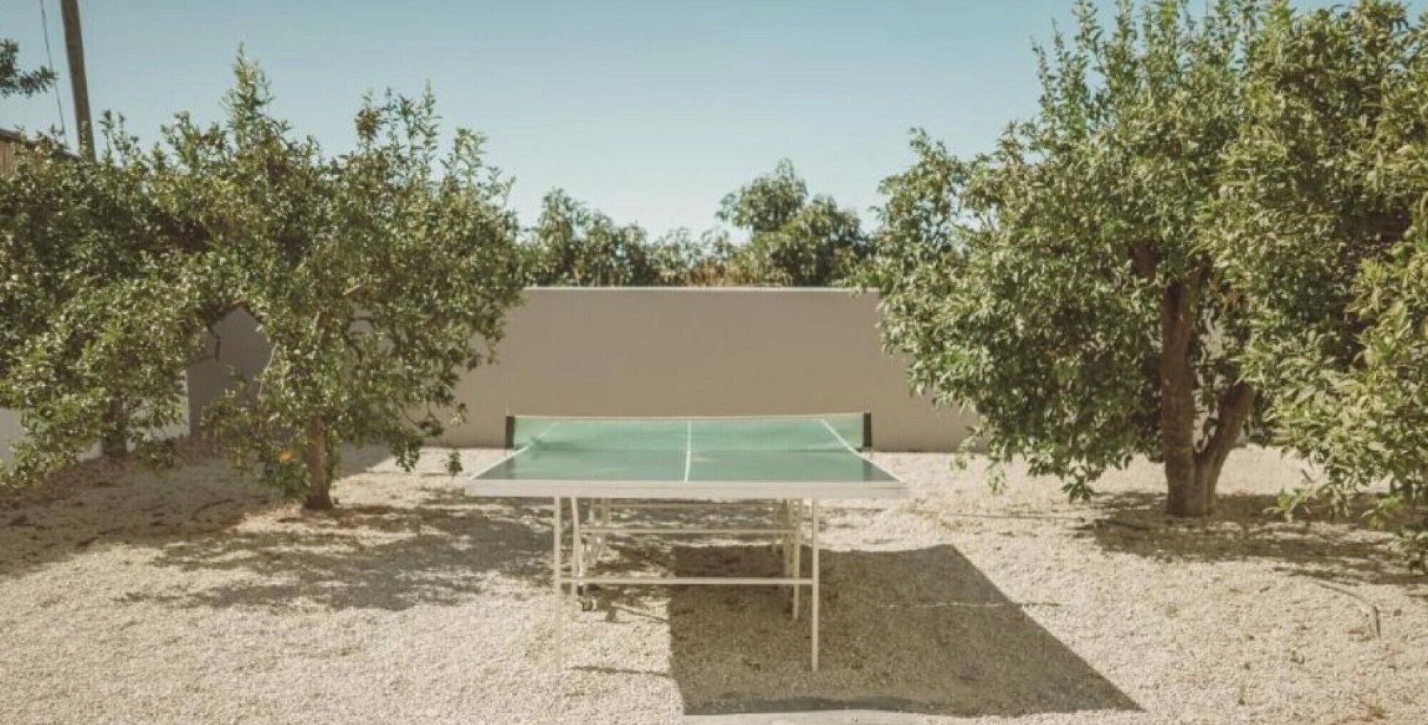 An outdoor tennis court with a net, surrounded by trees and a building in the background.