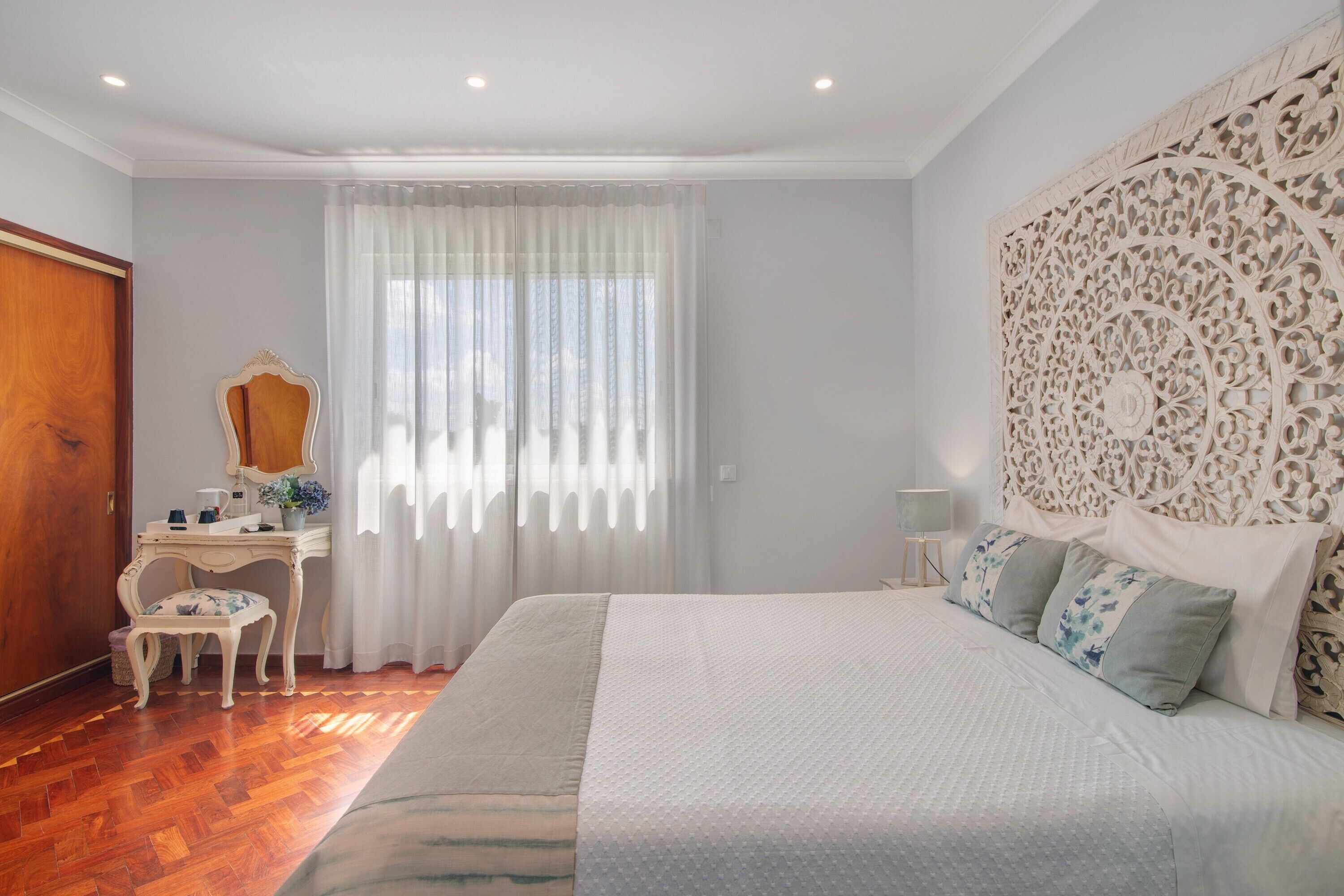 A bedroom with a large bed, a desk with a chair, a mirror, and a decorative headboard.