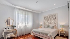 Ein Schlafzimmer mit Bett, Schminktisch mit Spiegel, Schreibtisch und einer dekorativen Wandgestaltung.