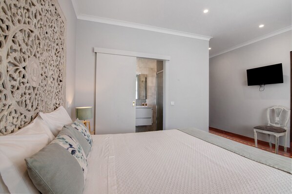 Un dormitorio con una cama grande, un televisor montado en la pared y una silla.