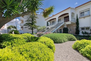 A multi-story building with a central staircase, surrounded by well-manicured hedges and a gravel path.