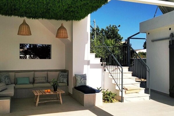 A modern outdoor living area with a sofa, a wooden table, and two hanging lamps.