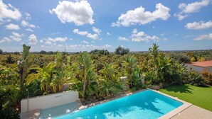 A swimming pool surrounded by lush greenery and a clear blue sky. - Milreu Guesthouse - Room 'Alecrim' (Estói)